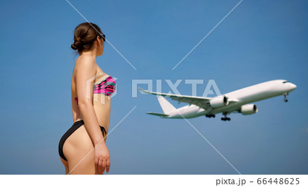 slim woman stands on beach watching flying past aircraft 66448625