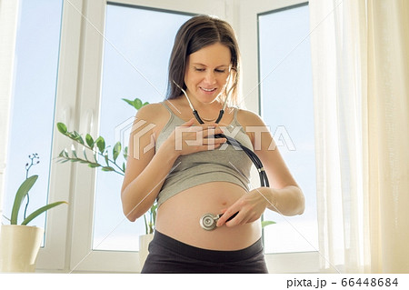 Beautiful young pregnant woman with stethoscope listening to her belly with baby 66448684