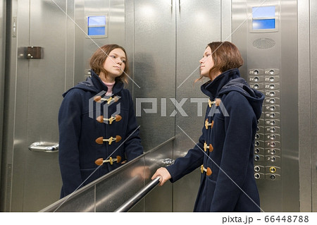 Teenage girl standing in elevator, looking in the mirror 66448788