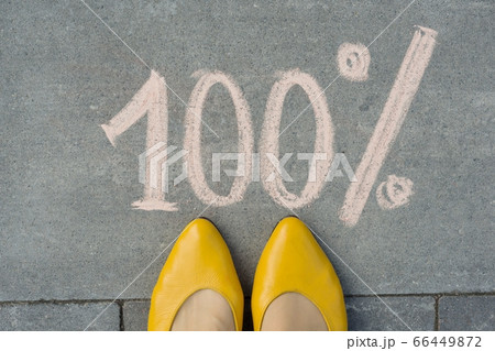 Female feet with text 100 percent written on grey sidewalk. 66449872