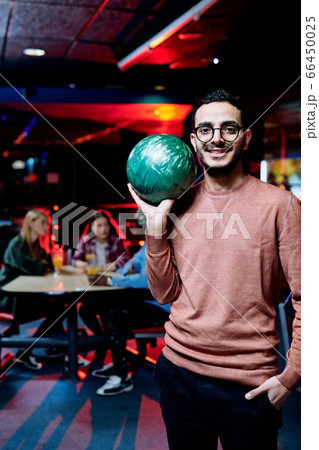 Happy mixed-race guy with green ball playing bowling at leisure center Happy mixed-race guy with green ball playing bowling at leisure center 66450025