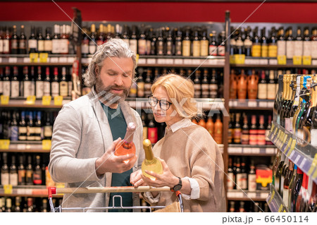 Aged bearded man with bottle of wine and his wife reading information on label Aged bearded man with bottle of wine and his wife reading information on label 66450114