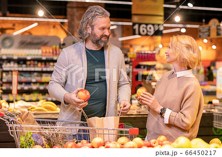 Happy mature man and his wife choosing fresh apples by display with fruits Happy mature man and his wife choosing fresh apples by display with fruits 66450217