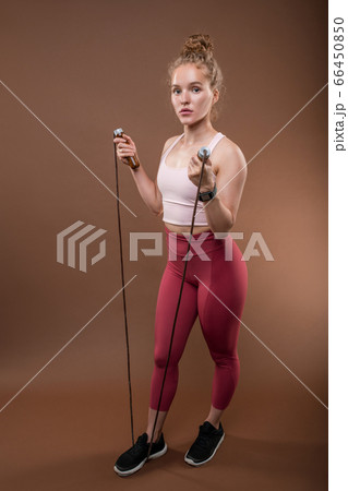 Pretty young fit sportswoman in activewear keeping right foot on skipping-rope Pretty young fit sportswoman in activewear keeping right foot on skipping-rope 66450850