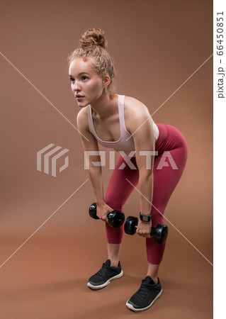 Young blond female athlete in activewear doing exercise for arms with dumbbells 66450851