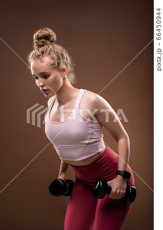 Young blond female in tracksuit bending slightly forwards while doing exercise 66450944