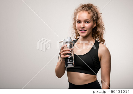 Happy young sportswoman in black activewear going to drink water after training Happy young sportswoman in black activewear going to drink water after training 66451014