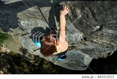 Top view on a pretty girl rock climber climbing up a cliff on a sunny day Top view on a pretty girl rock climber climbing up a cliff on a sunny day 66451023