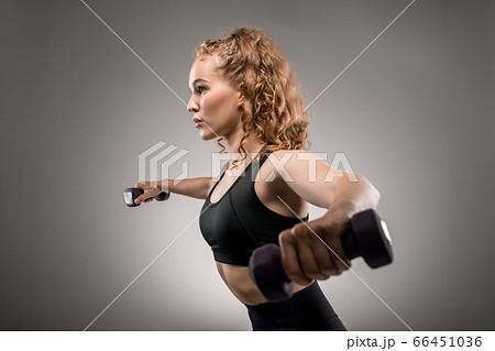 Side view of young sportswoman in tracksuit lifting dumbbells and breathing 66451036