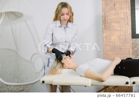 Cosmetology, massage therapy. Half length portrait of pretty blond Caucasian woman cosmetologist making face massage for her charming girl patient, in modern beauty center 66457781