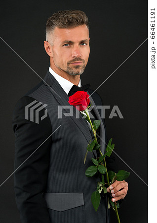 sexy man in black suit hold red rose. magician in 66461191