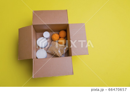 the main products for self-isolation in a box: cereals, buckwheat, fruit, canned food on a yellow background. home delivery. Assistance to population 66470657