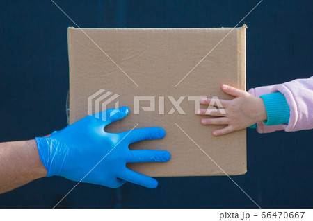 food delivery to your home. assistance to pensioners, the poor and the population. a courier in rubber gloves gives a box of food to a child. from hand to hand food delivery to your home. assistance to pensioners, the poor and the population. a courier in rubber gloves gives a box of food to a child. from hand to hand 66470667