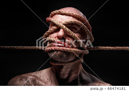 Image of binded bald man with rope on face 66474181