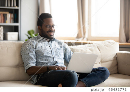 African man sitting on couch smile looking movie using laptop African man sitting on couch smile looking movie using laptop 66481771