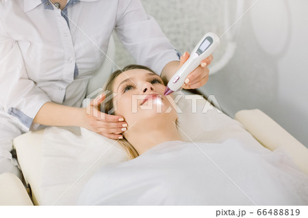Cropped image of female surgeon beautician removing pigmentation and vascular nets on the skin of the patient, beautiful young woman, using laser tool. Laser cosmetology Cropped image of female surgeon beautician removing pigmentation and vascular nets on the skin of the patient, beautiful young woman, using laser tool. Laser cosmetology 66488819