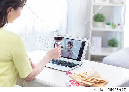 ノートパソコンでオンライン飲み会をする若い女性の後ろ姿の写真素材