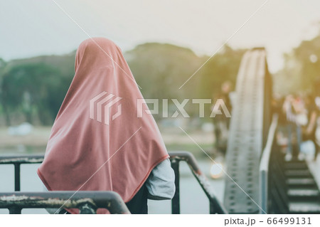 Back view of Muslim women relax and admire the beautiful scenery in the evening on The Bridge of the River Kwai in Kanchanaburi, Thailand. Back view of Muslim women relax and admire the beautiful scenery in the evening on The Bridge of the River Kwai in Kanchanaburi, Thailand. 66499131