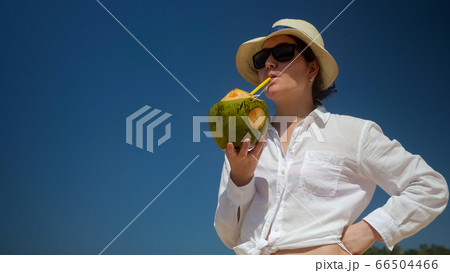 lady stands and drinks coconut with straw against blue sky lady stands and drinks coconut with straw against blue sky 66504466