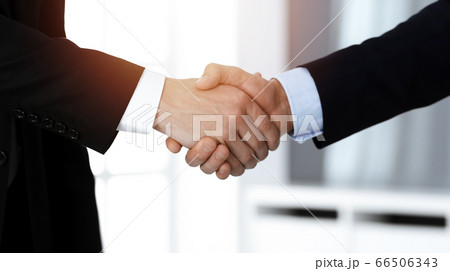 Business people shaking hands after contract signing while standing in sunny office. Teamwork and handshake concept 66506343