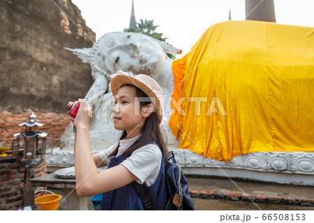 Cute happy smiling tourist girl taking photos with camera,Reclining Buddha background,at Wat Yai Chaimngkol, Ayutthaya,Thailand, summer vacation,travel concept. Cute happy smiling tourist girl taking photos with camera,Reclining Buddha background,at Wat Yai Chaimngkol, Ayutthaya,Thailand, summer vacation,travel concept. 66508153