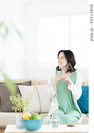 リビングでコップの水を飲むミドル女性 66513848
