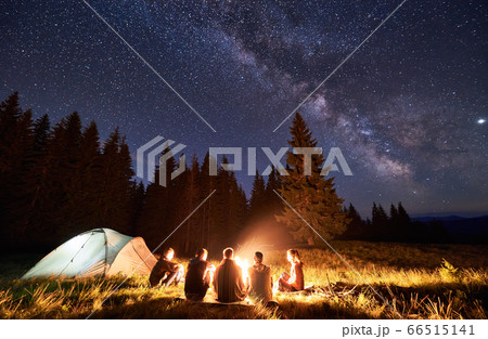 Tourists sitting around bonfire in night forest. 66515141