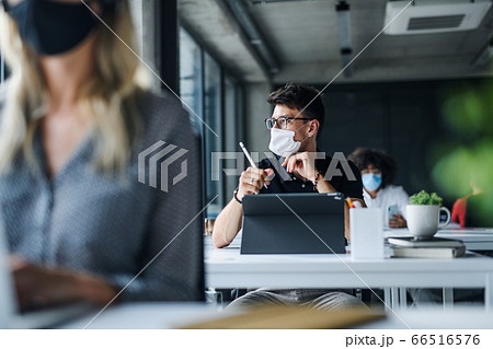 Young people with face masks back at work or school in office after lockdown. 66516576