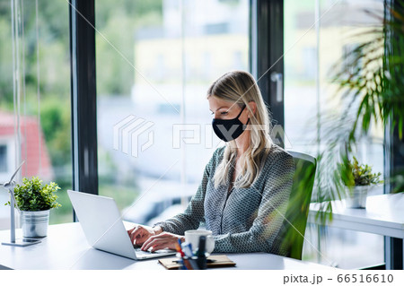 Young woman with face mask back at work in office after lockdown, using laptop. 66516610