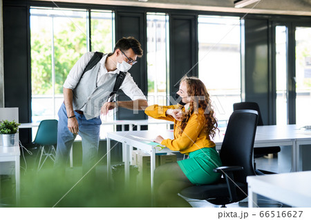 Young people with face masks back at work in office after lockdown, greeting. 66516627