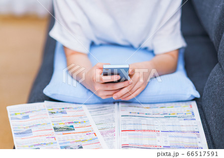 パンフを見ながらスマホで旅行計画を練る若い女性【アフターコロナのライフスタイル】 66517591