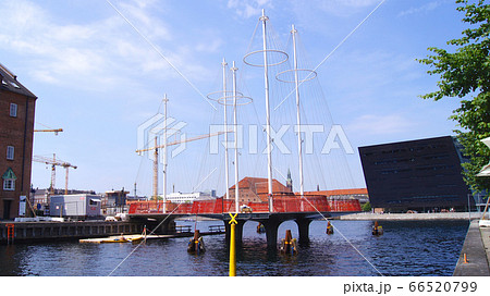 COPENHAGEN, DENMARK - JUL 05th, 2015: The new Circle Bridge with masts like a ship in Copenhagen harbor, against the shape of the Black Diamond, extension of the Royal Library 66520799