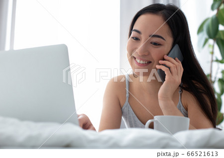 Happy woman communicating on cell phone in front of laptop Happy woman communicating on cell phone in front of laptop 66521613