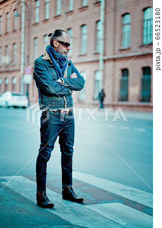 a man walks in the street, he has denim jacket, glasses, mustache and beard 66523180