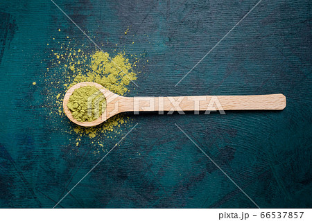 Wooden spoon filled with green matcha tea powder with a little bit powder spilled out on emerald backdrop. Japanese Matcha tea is luxury organic beverage rich of antioxidants. Top view. Copy space. 66537857