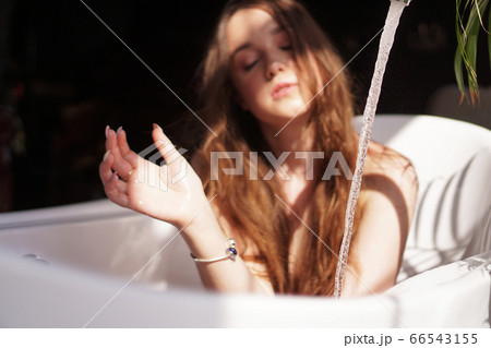 Blurry photo in defocus. Woman waits until the bathtub is filled with water Blurry photo in defocus. Woman waits until the bathtub is filled with water 66543155