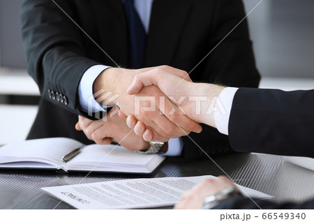 Businessman shaking hands with his colleague or partner above the glass desk in modern office, close-up. Unknown business people at meeting. Teamwork, partnership and handshake concept 66549340