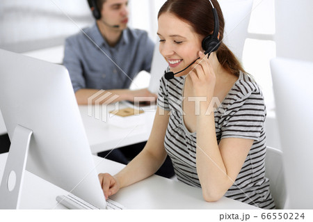 Group of operators at work. Call center. Focus on beautiful woman receptionist in headset at customer service. Business concept and casual striped clothing style 66550224