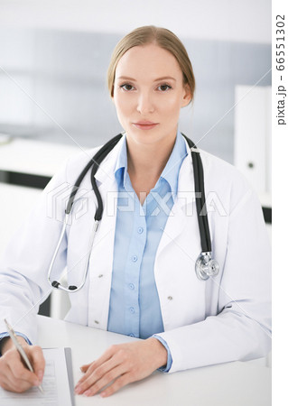Doctor woman filling up medication history records while sitting at the desk in hospital office. Physician woman at work. Data in medicine and healthcare Doctor woman filling up medication history records while sitting at the desk in hospital office. Physician woman at work. Data in medicine and healthcare 66551302