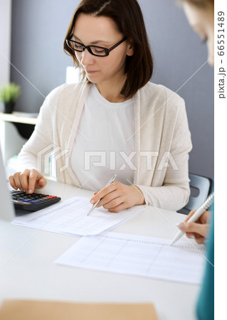 Accountant checking financial statement or counting by calculator income for tax form, hands close-up. Business woman sitting and working with colleague at the desk in office. Audit concept Accountant checking financial statement or counting by calculator income for tax form, hands close-up. Business woman sitting and working with colleague at the desk in office. Audit concept 66551489