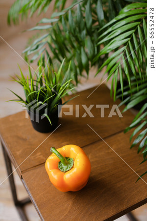 Orange ripe bellpepper lying on wooden table near houseplants. 66552478