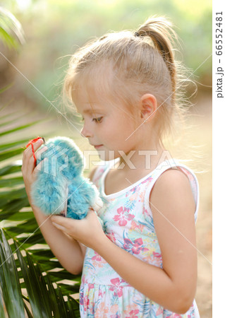 Little girl playing with toynear plam leaf outside. 66552481