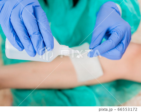 Close-up of a cotton swab and a bottle of antiseptic in the hands of a doctor against the background of a wound on the patient's leg. Close-up of a cotton swab and a bottle of antiseptic in the hands of a doctor against the background of a wound on the patient's leg. 66553172