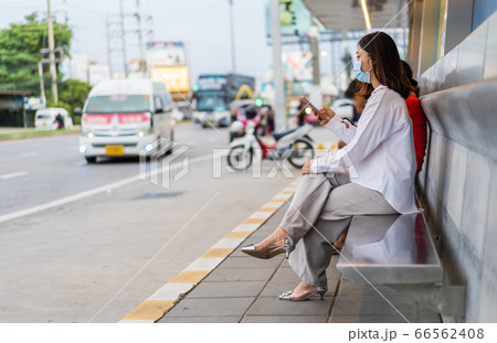 young woman holding smartphone and waiting for bus young woman holding smartphone and waiting for bus 66562408