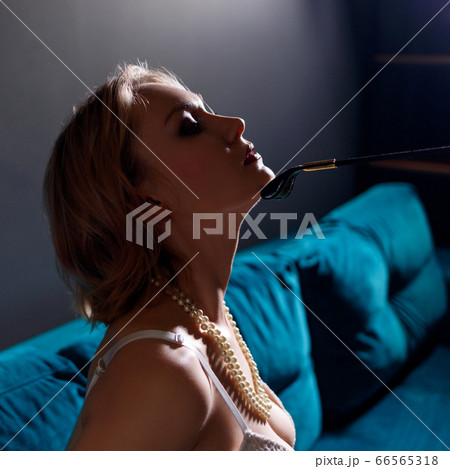 Blonde submissive woman sitting and leather whip touches her chin. 66565318