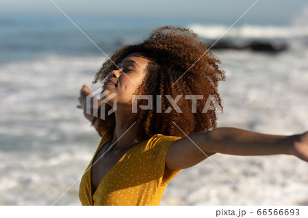A mixed race woman with her arms outstretched on beach on a sunny day 66566693