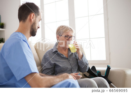Young caregiver sitting down on couch with senior woman Young caregiver sitting down on couch with senior woman 66569095