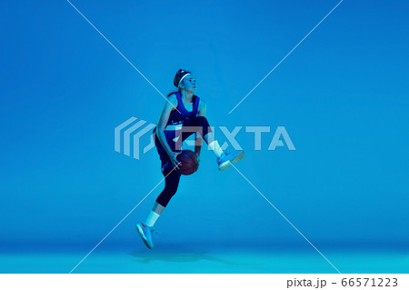 Young caucasian female basketball player isolated on blue studio background in neon light Young caucasian female basketball player isolated on blue studio background in neon light 66571223