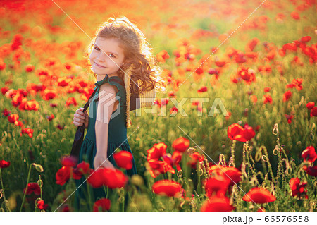 Cute little girl in green dress and straw hat posing at field of poppies on summer sunset Cute little girl in green dress and straw hat posing at field of poppies on summer sunset 66576558