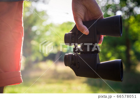 Male hiker looking through binoculars in forest Male hiker looking through binoculars in forest 66578051